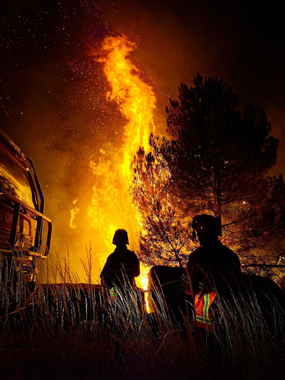 Firefighters battle a blazing wildfire at night, captured in dramatic silhouette.